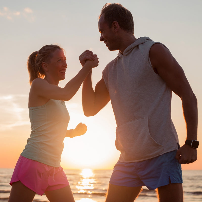 Two people arm-wrestling on a beach at sunset